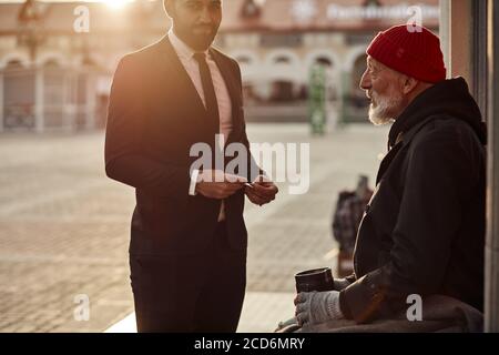 Young business man in suit help vagrant man in street, giving money donation. people relationship and lifestyle concept Stock Photo