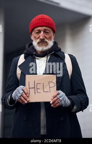 Old grey bearded man standing with sign HELP, asking for money, food, shelter. Concept of homeless person, poverty, despair Stock Photo