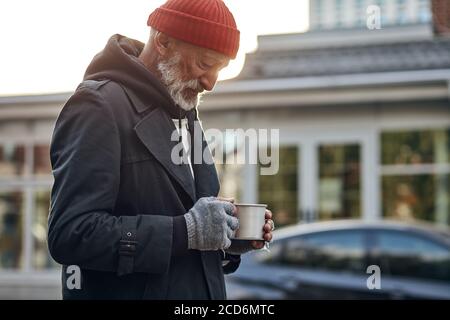 Penniless man collect money for shelter, food. Male desperately look at empty cup from coffee. Life depends on money. Homeless person on street Stock Photo