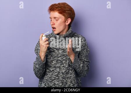 young man using inhaler. close up side view photo. isolated blue background, studio shot. Stock Photo