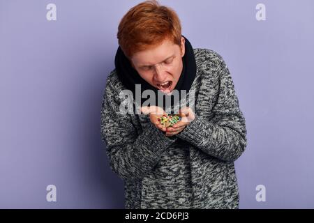 funny guy pretending that he is taking all pills lying on his plams. close up portrait, isolated blue background, studio shot Stock Photo