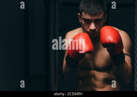 Strong muscular young boxer in sportswear training in dark studio, looks strong and powerful, warms up before game, building body and character Stock Photo