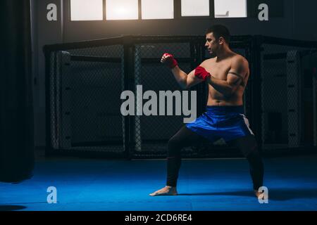 Martial arts of Muay Thai, Thai Boxing, Muay Thai. Barefoot Fighter training indoors dressed in blue boxer shorts and having his fists protected with Stock Photo