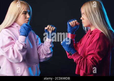 Women s kickboxing bout contested in the lightweight division. Two blonde sisters, sparring partners in blue handwraps and pink and white hoodie stand Stock Photo