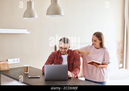 Cheerful young woman dressed in casual clothes, has positive emotions, smiles happily, looks at handsome boyfriend with toothy smile, puts hand on wid Stock Photo