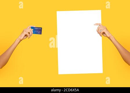 Female hands holding empty white billboard paper and credit cards on isolated studio yellow bakground Stock Photo