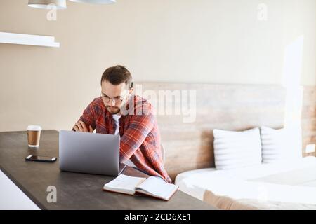 Concentrated busy freelancer sitting alone in living room, looking at laptop computer, focusing in device with puzzled expression, portrait, indoor sh Stock Photo