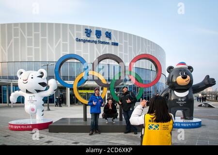 Gangneung, South Korea - Tourists posing for a picture with the Olympic flag and 2018 Pyeongchang Winter Olympics mascots in front of train station. Stock Photo