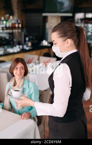 A European-looking waiter in a medical mask serves Latte coffee Stock ...