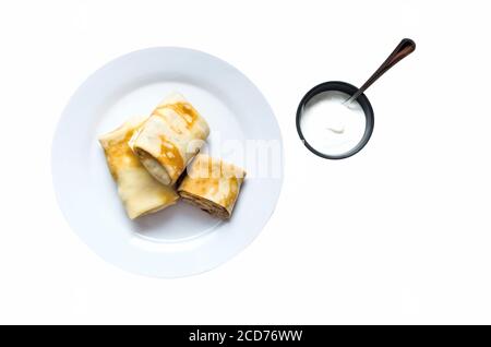 Pancakes stuffed on a plate with sour cream isolated on white background Stock Photo