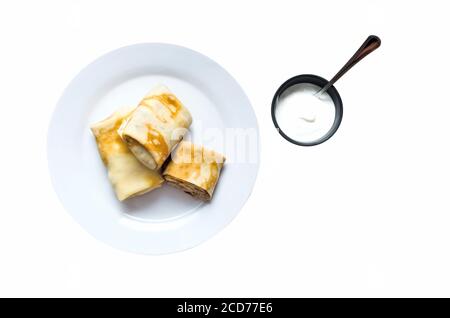 Pancakes stuffed on a plate with sour cream isolated on white background Stock Photo