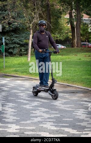 A man wearing a safety helmet & neck scarf rises his Nanrobot electric scooter on a path in Kissena Park in Flushing, Queens, New York City. Stock Photo