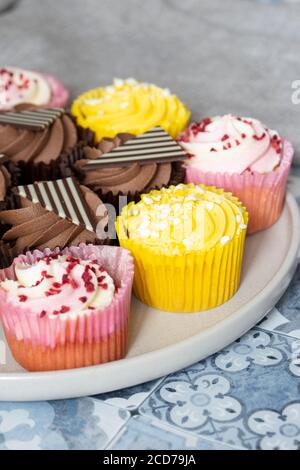 Variety of cupcakes on a grey plate.  Blue patterned tile background Stock Photo