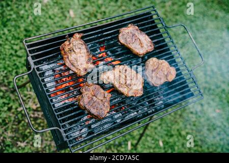 Five steaks are fried on charcoal on a metal grill.  Stock Photo