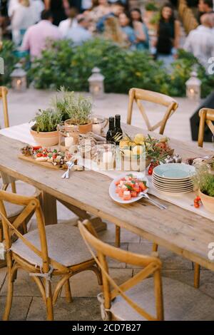 A festive table with fresh flowers in pots and lemons in a deep plate in a restaurant with chairs and guests on a blurred background. Stock Photo