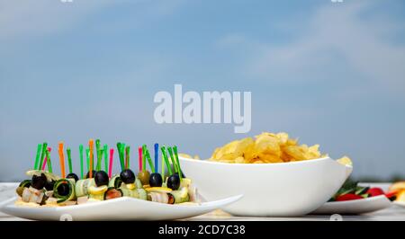 Canapes with olives, cucumber and beef brisket. Potato chips on white bowl. Stock Photo