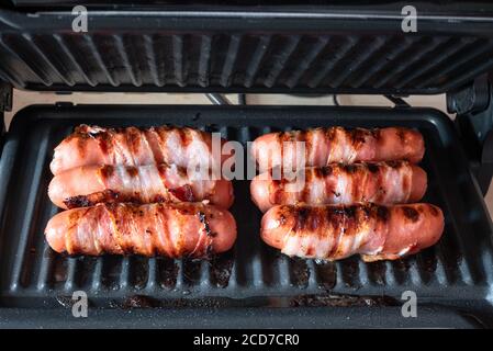 Appetizing sausages wrapped in bacon are grilled on a electric grill Stock Photo