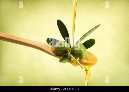 Olive oil falling on wooden spoon with raw olives with olive leaves with isolated green background. Stock Photo
