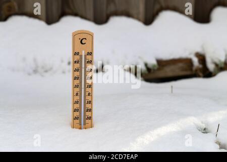 Selective focus shot of a  wooden thermometer standing in the snow Stock Photo