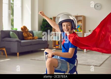 Superhero child. Kids costume. Children's room. Child boy in red cape and superhero helmet plays in nursery. Stock Photo