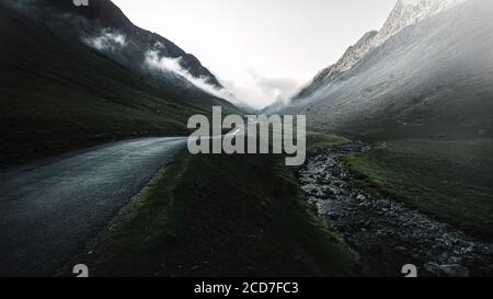 Moody image of Honister pass in Lake District, Cumbria, UK.Fog in mountain valley with country road and stream.
