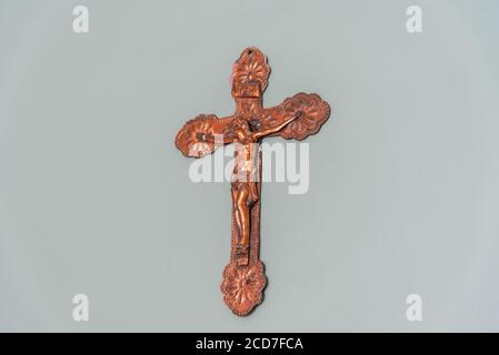 Image of an old crucifix hanging on the masonry wall made of galvanized iron and artificially aged. Religious artifact. Symbol of the Catholic Church Stock Photo