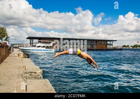 ISTANBUL / TURKEY - 07.17.2020: Young turkish man jumping in the sea from the pier of Karakoy on a hot summer day, the Golden Horn, Istanbul, Turkey.