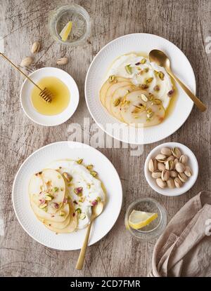 Ricotta with pears, pistachios and honey or maple syrup on two white plate Stock Photo