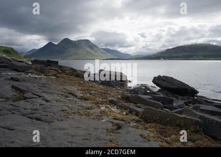 Coastal landscape from the isle of raasay looking towards the isle of skye. Ferry travels the sea under the peak of Glamaig which is cloud topped. Stock Photo