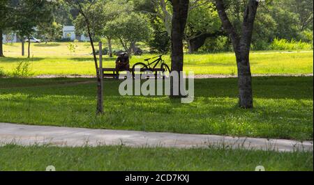 A young man sitting in the shade of the park playing with his cell phone. Beside you, the bicycle that is your means of transport. Urban scene and the Stock Photo
