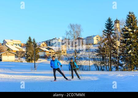 Two skiers doing a skating exercise in late winter afternoon near a village Stock Photo
