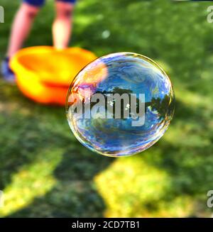 A soap bubble flies against the background of green grass. Bubbles of air on a sunny summer day outdoors. Stock Photo