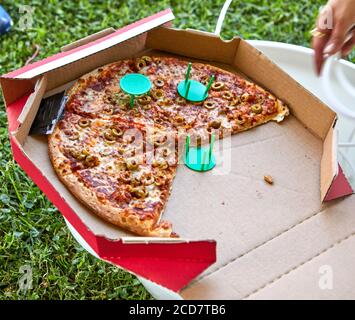 Italian pizza with tomato sauce in opened cardboard box on the grass in the city park. Food delivery concept Stock Photo