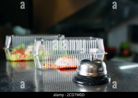 food delivery. distribution table in a restaurant with a metal bell. food in plastic containers. Panna cotta and vegetable salad in a plastic Stock Photo