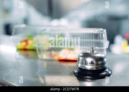 food delivery. distribution table in a restaurant with a metal bell. food in plastic containers. Panna cotta and vegetable salad in a plastic Stock Photo