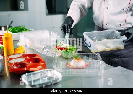 Food delivery in the restaurant. The chef prepares food in the restaurant and packs it in disposable dishes. Stock Photo