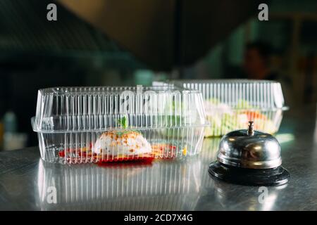 food delivery. distribution table in a restaurant with a metal bell. food in plastic containers. Panna cotta and vegetable salad in a plastic Stock Photo