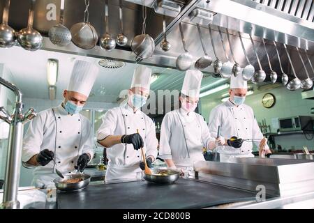 Chefs in protective masks and gloves prepare food in the kitchen of a restaurant or hotel. Stock Photo