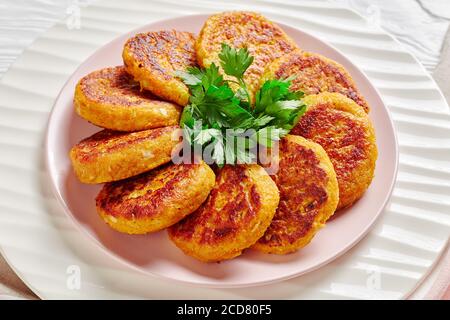 Curried vegan butternut squash fritters on a white plate with parsley served on white wooden background, top view, close-up Stock Photo