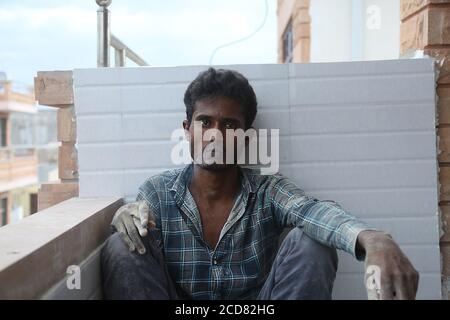 jodhpur, rajasthan, india, 20th September 2020: Young indian male labour worker smoking cigarette wearing dirty clothes while sit relaxing against the Stock Photo