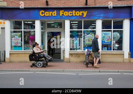 A middle aged woman in a motorized wheelchair outside of the card factory shop Stock Photo