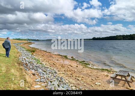 A couple of people along the lake shore on a cloudy, windy day at the reservoir of Rutland, England. Stock Photo