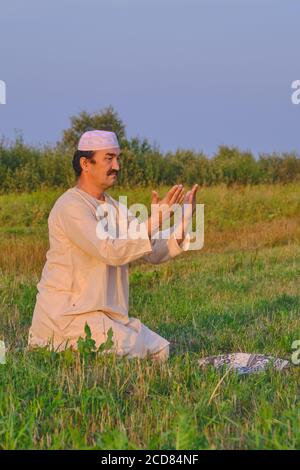 A muslim senior man wearing a skullcap and traditional clothes prays Portrait of a cute young black bull on a pasture Stock Photo