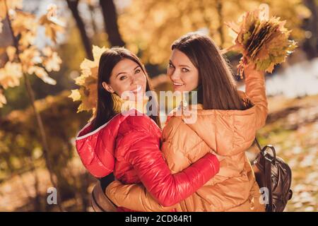 Back rear spine view photo of positive cheerful forever friends girls hug embrace enjoy rest relax in fall forest park collect hold maple leaves wear Stock Photo