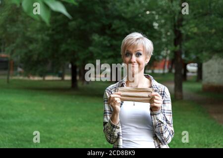 young blonde woman holding a disposable mask in her hands and smiling. end of mask mode. victory over the virus Stock Photo