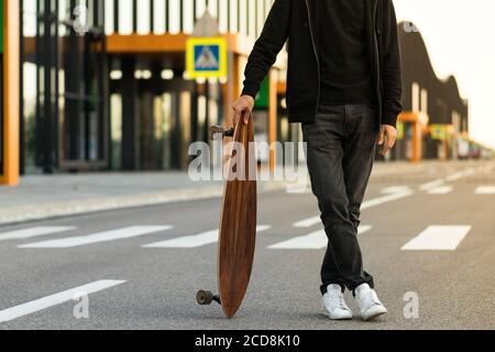 Man hipster standing with skateboard or longboard outdoors, cropped image. Leisure, healthy lifestyle, extreme sports Stock Photo