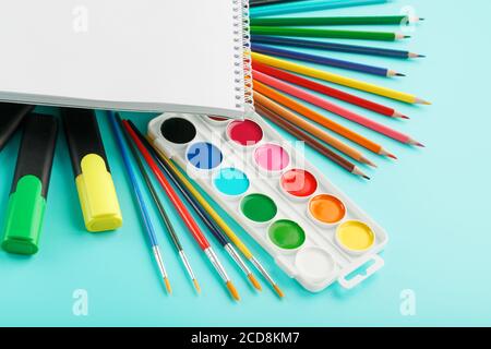 An album for creative development at school, with stationery on a cyanide background. A palette of colored paints, markers, brushes and pencils. Stock Photo