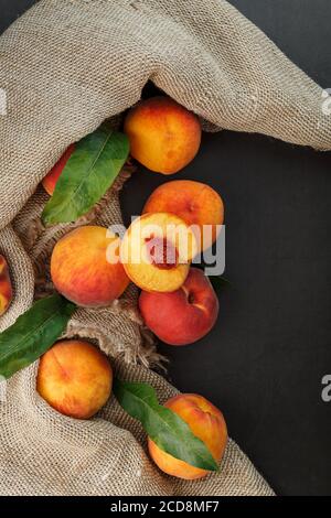 Peach fruit on a black background with a cloth of burlap and green leaves. Stock Photo