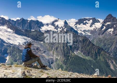 Man on the edge of the abyss against the background of mountain peaks in the snow and blue sky with clouds, summer sunny day Stock Photo