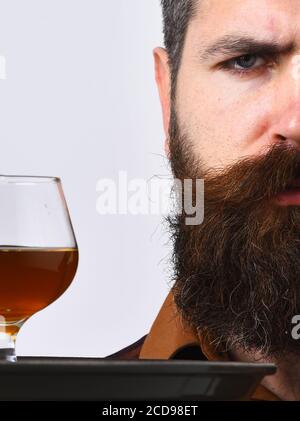 Waiter with glass and bottle of whiskey on tray. Service and expensive beverage concept. Man with beard holds alcohol on white background, close up. Barman with serious face serves scotch or brandy. Stock Photo